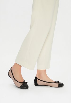 Czarne i cieliste baletki z okrągłymi noskami, akcentem w postaci kokardy oraz płaską podeszwą, wykonane z gładkich materiałów. Noszone z luźnymi, jasnymi spodniami.