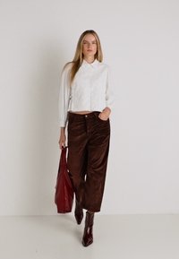Witte cropped blouse met een knopkraag, bruine corduroy wijde broek, en bijpassende bordeauxrode tas en laarzen. Gladde texturen zichtbaar.