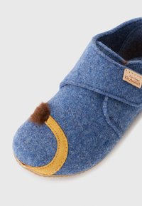 Chinelo de feltro azul com destaque em couro amarelo, ponta redonda e detalhe em pele sintética castanha. Apresenta uma etiqueta de logo bordada. Material macio e texturizado.
