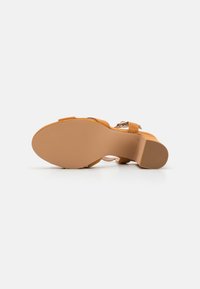 Brune semsket høyhælte sandaler med et elegant stroppdesign, rund tå og teksturert gummisåle for grep. Spenne-dekordetalj inkludert.