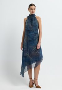 Vestido azul asimétrico con escote halter y tela drapeada que presenta un patrón de paisley. La textura suave y fluida complementa el diseño.