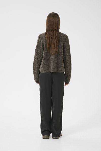 Un pull en tricot marron avec une coupe décontractée, associé à un pantalon noir ample et des chaussures vertes, vu de dos sur un fond clair.