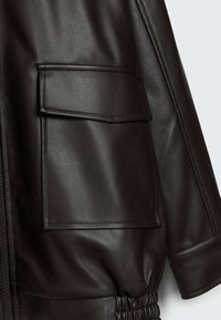 Brązowa skórzana kurtka z dużą kieszenią na klapie, teksturowanym wykończeniem i marszczonym elastycznym dołem. Gładki materiał o zorganizowanej strukturze.