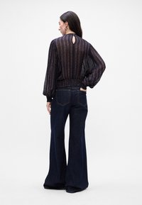 Blusa navy con righe verticali, dettaglio a fessura sul retro e vita elasticizzata, abbinata a jeans in denim scuri a zampa.