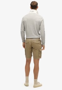 Un haut gris à manches longues avec un col montant, associé à un short cargo beige clair avec des poches. Des chaussettes beige clair et des chaussures complètent la tenue.