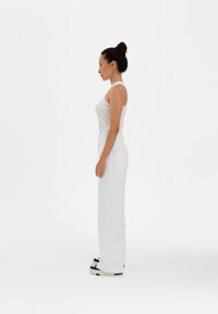 White sleeveless tank top paired with white wide-leg pants. The pants feature a side pocket; model stands in profile against a plain background.