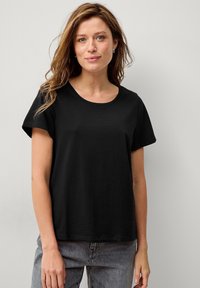 Schwarzes Baumwoll-T-Shirt mit kurzen Ärmeln und rundem Halsausschnitt, im lässigen Schnitt und mit glatter Textur. Trägt man mit grauen Jeans.
