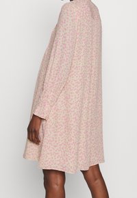 Sukienka w panterkę z miękkiej, lekkiej tkaniny. Posiada długie rękawy, luźny krój oraz różowy wzór na jasnobeżowym tle.