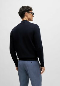 Cardigan lavorato a maglia blu navy con maniche lunghe e orlo a coste, abbinato a pantaloni leggeri blu chiaro con un motivo, dotati di tasca posteriore e dettaglio con bottone.