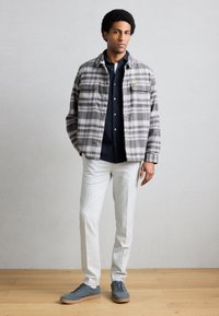 Γκρι και λευκό καρό σακάκι, μπλε πουκάμισο, ανοιχτόχρωμο παντελόνι και γκρι αθλητικά παπούτσια με καφέ σόλες. Δύο μπροστινές τσέπες στο σακάκι.