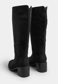 Botas de ante negras hasta la rodilla con un tacón ancho, que presentan una textura suave, cierre lateral con cremallera y una parte superior ligeramente puntiaguda.