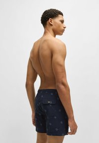 Navy swim shorts with a patterned design, made from lightweight fabric. Features an elastic waistband and a back pocket with hardware detail.