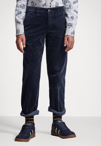 Marineblauwe corduroy broek met een rechte snit, voorzien van een knoopsluiting, opgerolde manchetten, en gecombineerd met marineblauwe sneakers en gestreepte sokken.