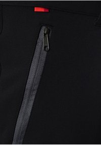 Svart tyg med en slät textur har en sidodragkedja i mörkgrått och en liten röd detalj vid midjan.