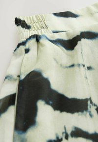 Tissu léger avec une taille élastique, présentant un motif abstrait noir et bleu sur un fond pâle. Texture douce et finition lisse.
