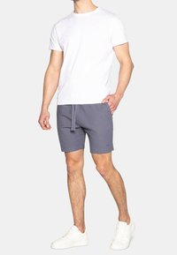Szare szorty kąpielowe z elastycznym paskiem, w połączeniu z dopasowaną białą koszulką i białymi sneakerami. Tkaniny wyglądają na gładkie i swobodne.