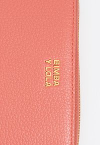 Billetera de piel coral con superficie texturizada y logo dorado "BIMBA Y LOLA". Detalle de cierre con cremallera a lo largo del costado.