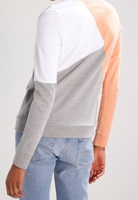 Sweatshirt s barevným dělením obsahující bílé, šedé a broskvové části. Vyrobeno z měkké tkaniny s kulatým výstřihem a žebrovanými manžetami. Volný střih.