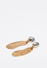 Złote kolczyki o młotkowanej fakturze, z wydłużonymi, zakrzywionymi kształtami i srebrnymi okrągłymi wkrętami.