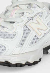 Κοντινή λήψη άσπρου αθλητικού παπουτσιού New Balance με λεπτομέρειες από δίχτυ και δέρμα, λευκά κορδόνια και μαύρη σόλα.
