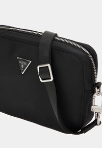 Black nylon purse with a rectangular shape, featuring a silver zipper, adjustable strap, and a metal logo accent on the side.