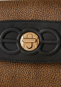 Materiale marrone con motivo testurizzato e pattina in pelle nera; presenta una chiusura circolare dorata con un logo e dettagli decorativi.