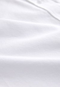 Detail hladkej bielej látky s jemnými záhybmi a jemnou textúrou.