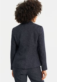 Mörkgrå skräddarsydd kavaj med en texturerad yta, utrustad med slagkrage, enkel bakventil och en strömlinjeformad siluett.