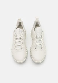 Chaussures de sport blanches avec dessus en mesh, lacets texturés et semelles épaisses en caoutchouc. Équipées de cols rembourrés et de détails de couture contrastants.