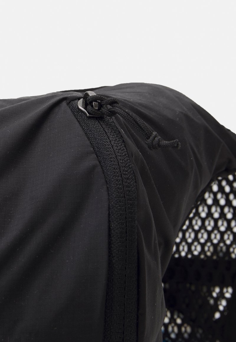 Zaino nero con chiusura a zip, tessuto texturizzato e pannello laterale in rete per la ventilazione. Dettaglio con cordoncino vicino alla parte superiore.