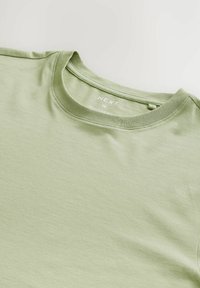 Tricou scurt cu mânecă scurtă de culoare verde deschis, realizat dintr-un material moale. Previne un guler rotund și eticheta cu textul "NEXT M REGULAR FIT."