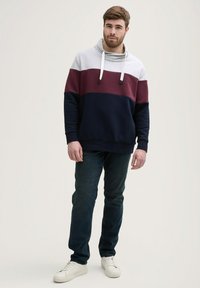 Felpa con cappuccio in grigio, bordeaux e blu navy. Tessuto morbido con design a blocchi di colore. Coulisse regolabile. Abbinata a jeans scuri e sneakers bianche.
