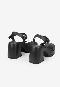 Las sandalias de plataforma negras cuentan con un amplio tacón de bloque, dos correas ajustables y una plantilla texturizada. Diseño minimalista con material sintético suave.
