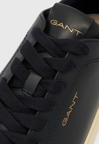 Marineblaue Ledersneaker mit strukturierten Stoffschnürsenkeln, goldfarbenem Markenlogo auf der Zunge und einer cremefarbenen Sohle. Klassisches Design mit minimalen Akzenten.