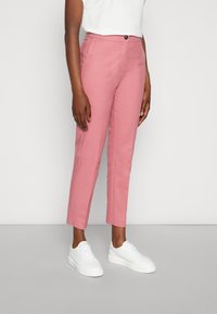 Rosa byxor med en skräddarsydd passform, som har en enkel knäppning med knapp och sidofickor, ihop med vita sneakers. Slät tygstruktur.