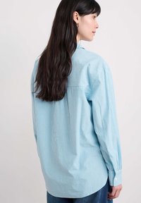 Lichtblauw gestreept shirt met lange mouwen, een knoopkraag en een afgeronde zoom. Zachte stof met een ontspannen pasvorm. Eenvoudige ontwerpelementen.