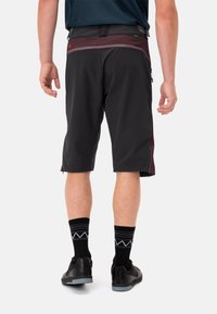 Pantaloni corti neri con una vita bordeaux, dotati di tasche laterali con zip e una vestibilità comoda, abbinati a calze e scarpe nere.