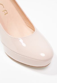 Escarpin en cuir verni rose clair avec un bout arrondi, une finition lisse et brillante, et une subtile couture le long du bord de la semelle.