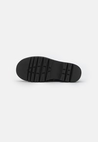 Semelle de chaussure en caoutchouc noir avec un motif de crampons profonds et des rainures pour l’adhérence. Texture lisse et design d’arête arrondie.