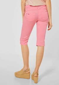 Pantaloni capri di denim rosa con tasche posteriori, abbinati a sandali con zeppa beige dotati di una fascia e texture intrecciata.