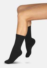 Schwarze Baumwollsocken mit einem gerippten Design und weicher Textur, die knapp oberhalb des Knöchels auf einem hellgrauen Hintergrund liegen.