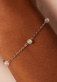 Zilveren kettingarmband met gladde witte kralen, die een verfijnd ontwerp en subtiele textuur toont tegen een achtergrond van een bruine huid.