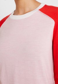 Różowo-czerwony top z rękawami raglanowymi i okrągłym dekoltem; miękka faktura i lekka tkanina; kontrastowe detale kolorystyczne na rękawach.