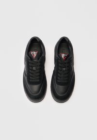 Une paire de baskets Guess noires avec un laçage à l'avant et un logo triangulaire rouge sur la languette, vues de dessus sur un fond blanc.