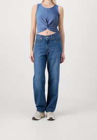 Haut court bleu à côtes avec un design en torsade, associé à un jean droit taille haute bleu et des baskets grises.