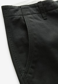 Pantalons en coton noir avec une texture lisse, poches latérales inclinées et un intérieur de ceinture en contraste blanc. Design ajusté avec des coutures visibles.