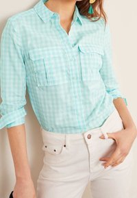 Light blue gingham checked shirt with long sleeves, two chest pockets, and button closure, paired with white pants. Smooth cotton fabric.