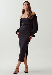 Schwarzes, schulterfreies Kleid mit langen Puffärmeln, figurbetont, mittellang mit einem Seitenschlitz, glattes Material und minimalistischem Design.