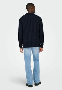 Marineblauer Kabelstrickpullover mit geripptem Kragen und Bündchen, kombiniert mit hellblauen geraden Jeans und schwarzen Schuhen.