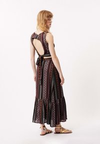 Maxikleid mit ausgeschnittenem Rücken, mehrfarbigen geometrischen Mustern, fransigem Saum und einer Bindegürtellinie. Hergestellt aus leichtem Stoff.